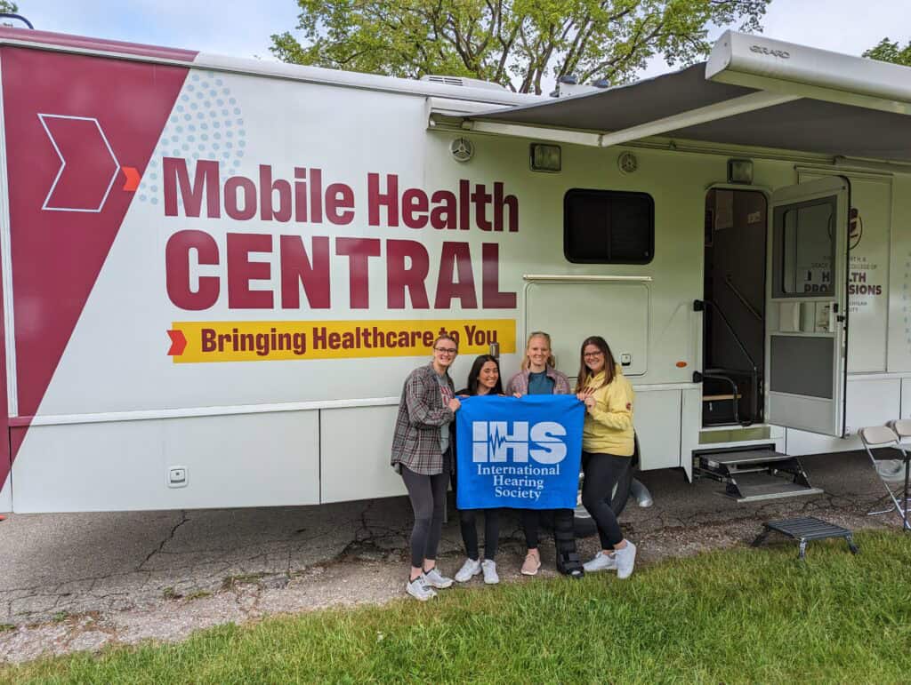 Central Michigan University students pose in front of the Mobile Health bus with the International Hearing Society flag