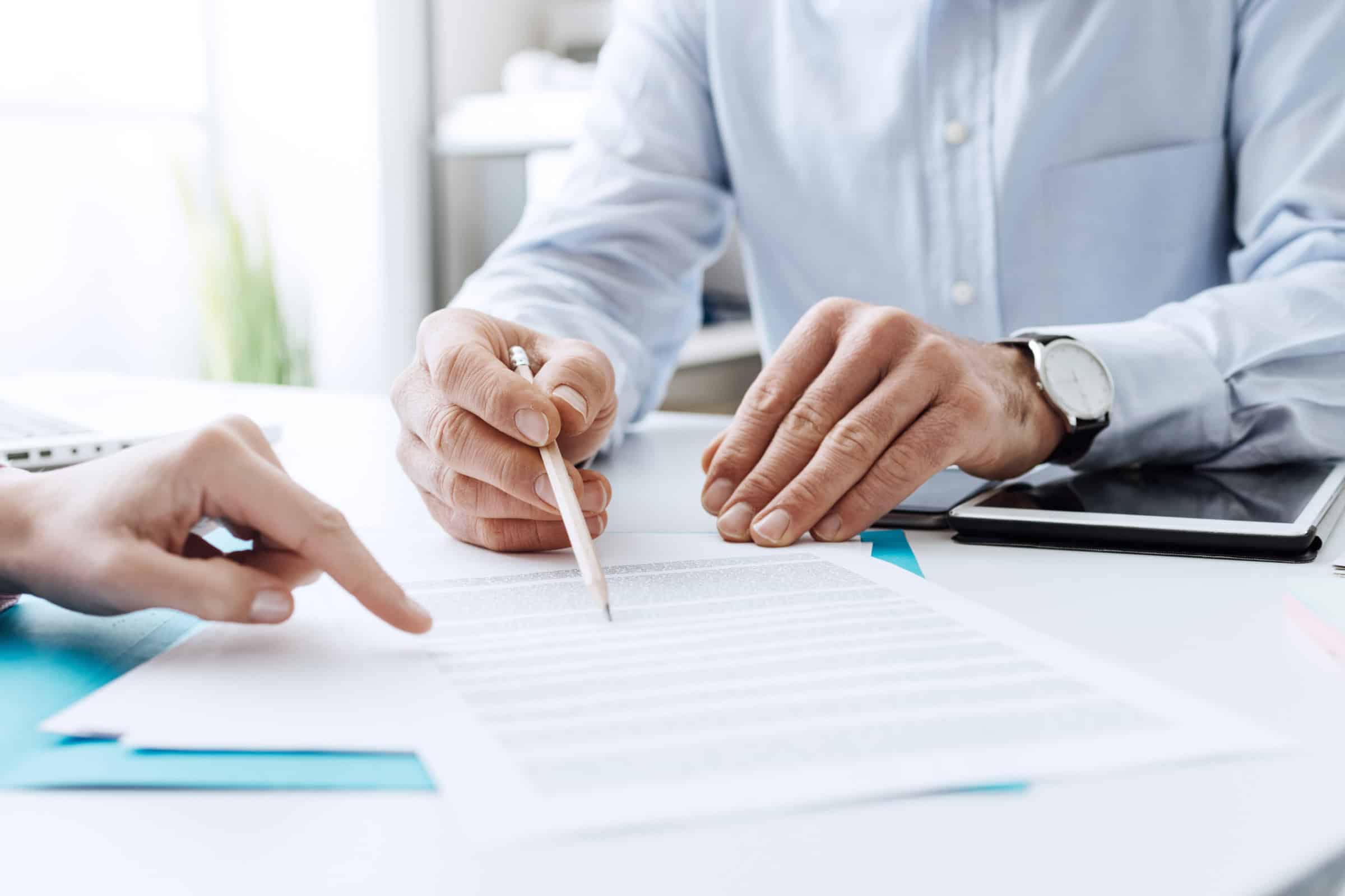 Two people review paperwork together, with one pointing at the document while the other holds a pen.