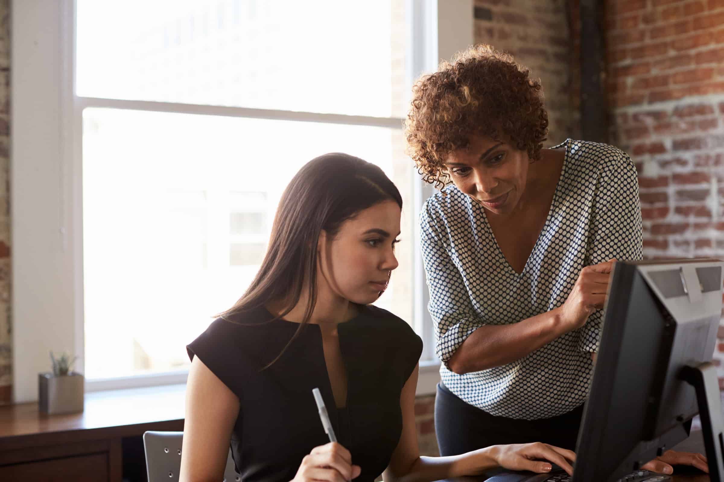 Two coworkers review information together on a computer screen