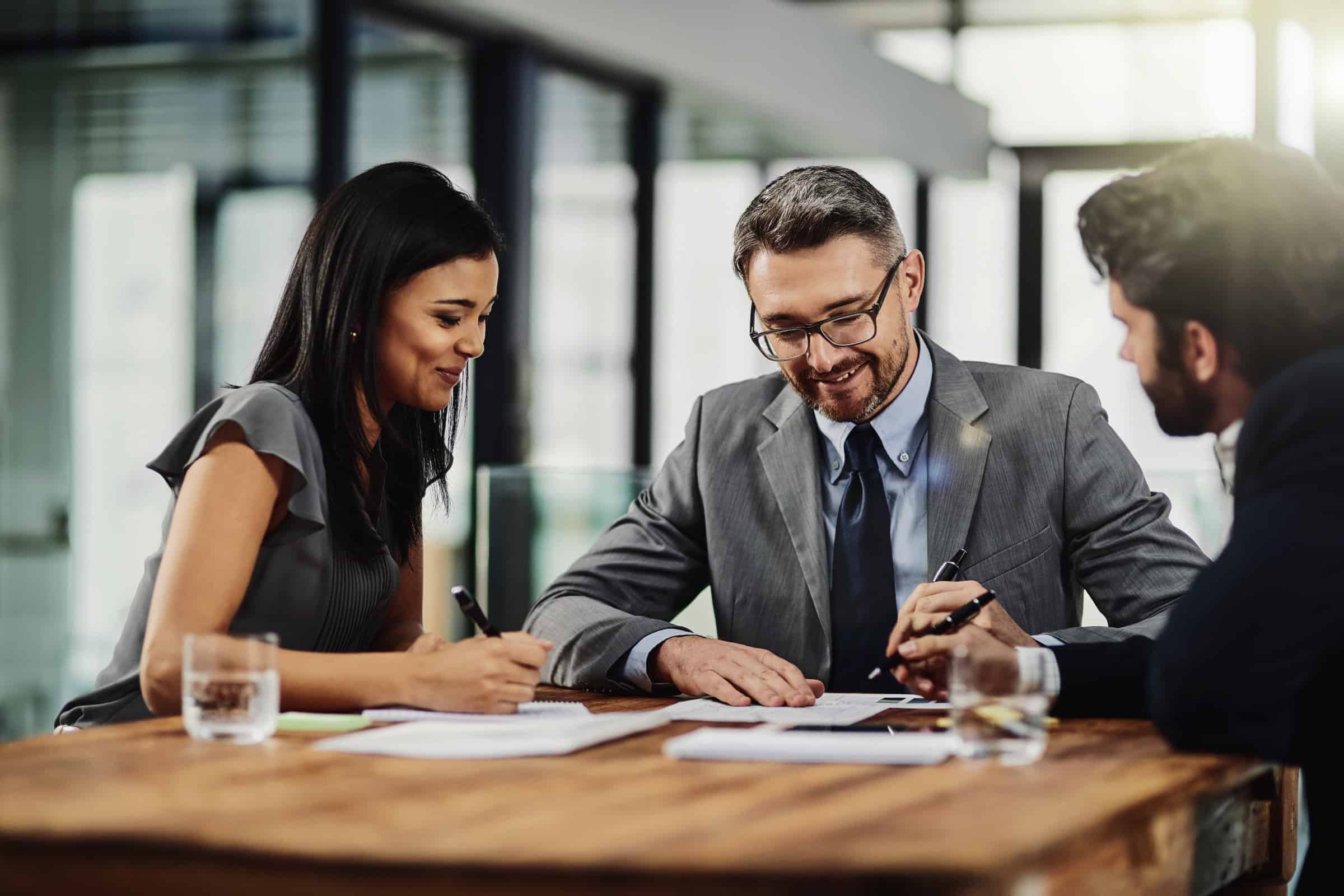 Three people around an office table with documents and smiling 