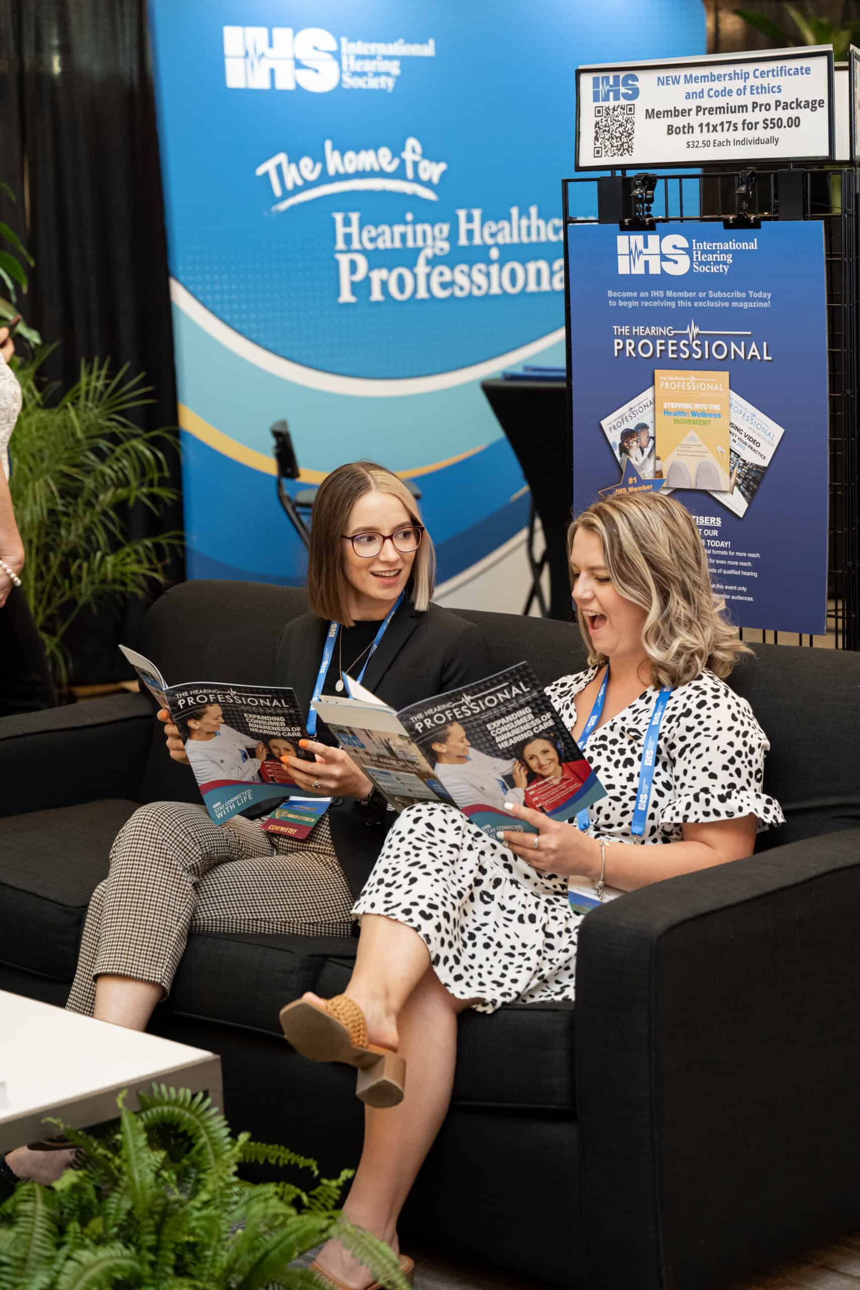 Two attendees read magazines at a conference booth.