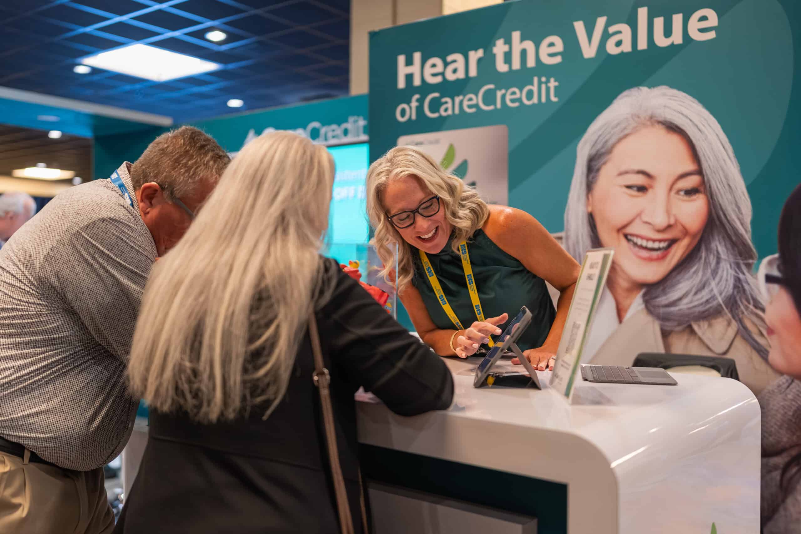 Exhibitor points to a screen demonstrating something for two expo attendees.