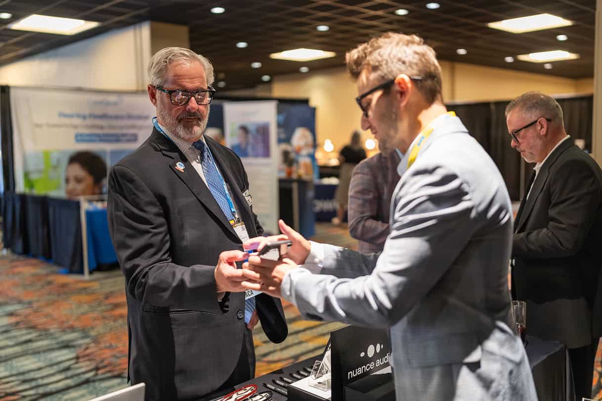 Two professionals discuss and examine a phone at an exhibitor booth during a conference expo.