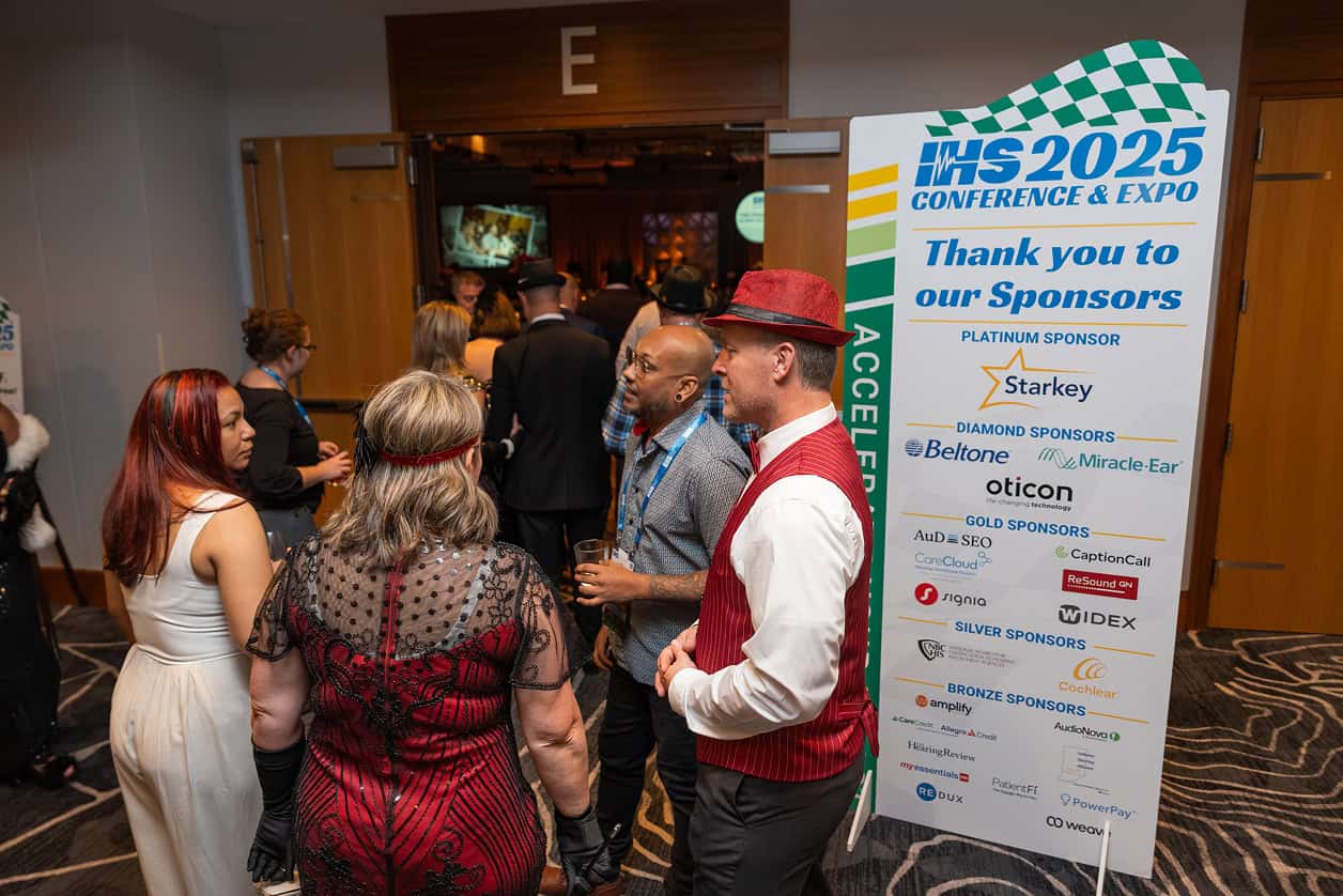 Attendees in formal and themed attire gather and talk outside a ballroom entrance at a conference networking event, standing beside a large sign thanking sponsors of the IHS 2025 Conference & Expo.