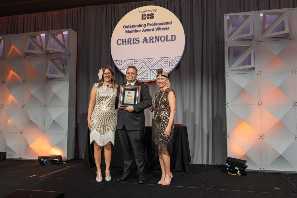 2025 Outstanding Professional Member Award Winner, Chris Arnold, accepting his award on stage with Executive Director, Alissa Parady, CAE, and President-Elect, Leanne Polhill, BA, BC-HIS