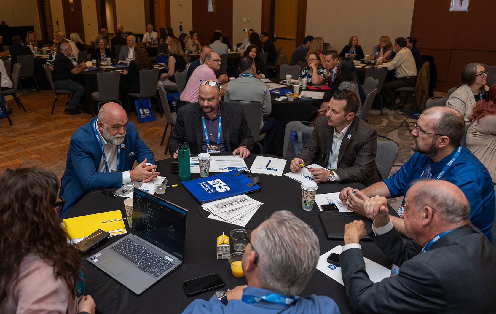 Conference attendees sit at round tables, discussing ideas and taking notes during a small-group session.