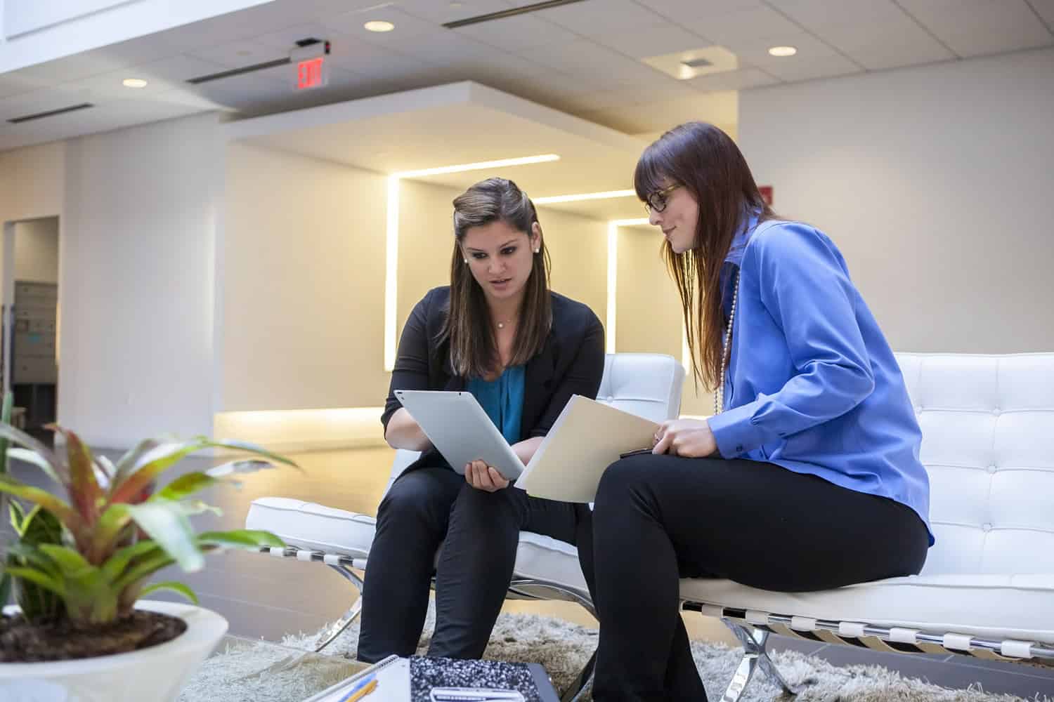 two professionals collaborating using a tablet in a large open office space.
