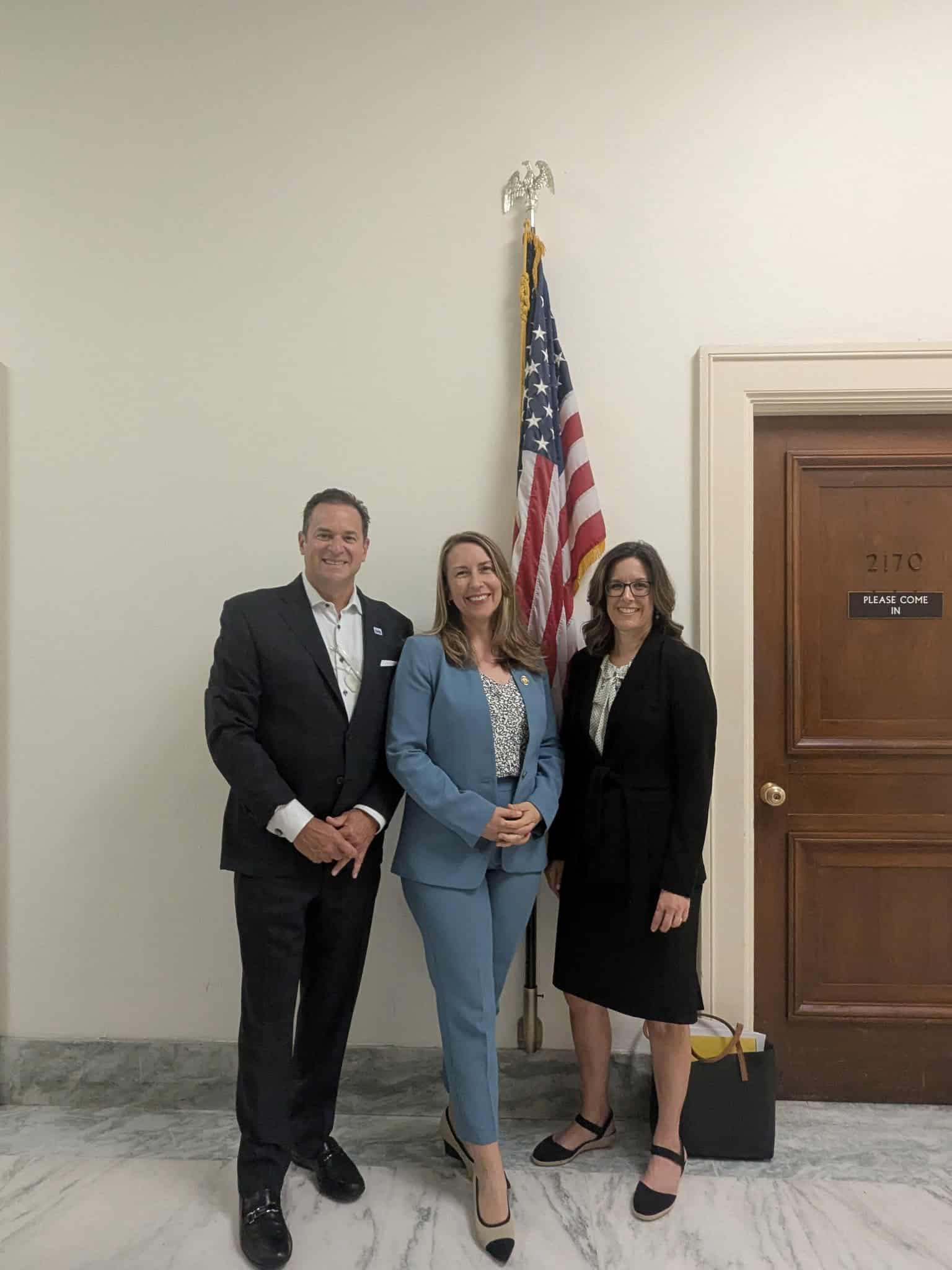 Three IHS representatives stand together in a government office near a U.S. flag.