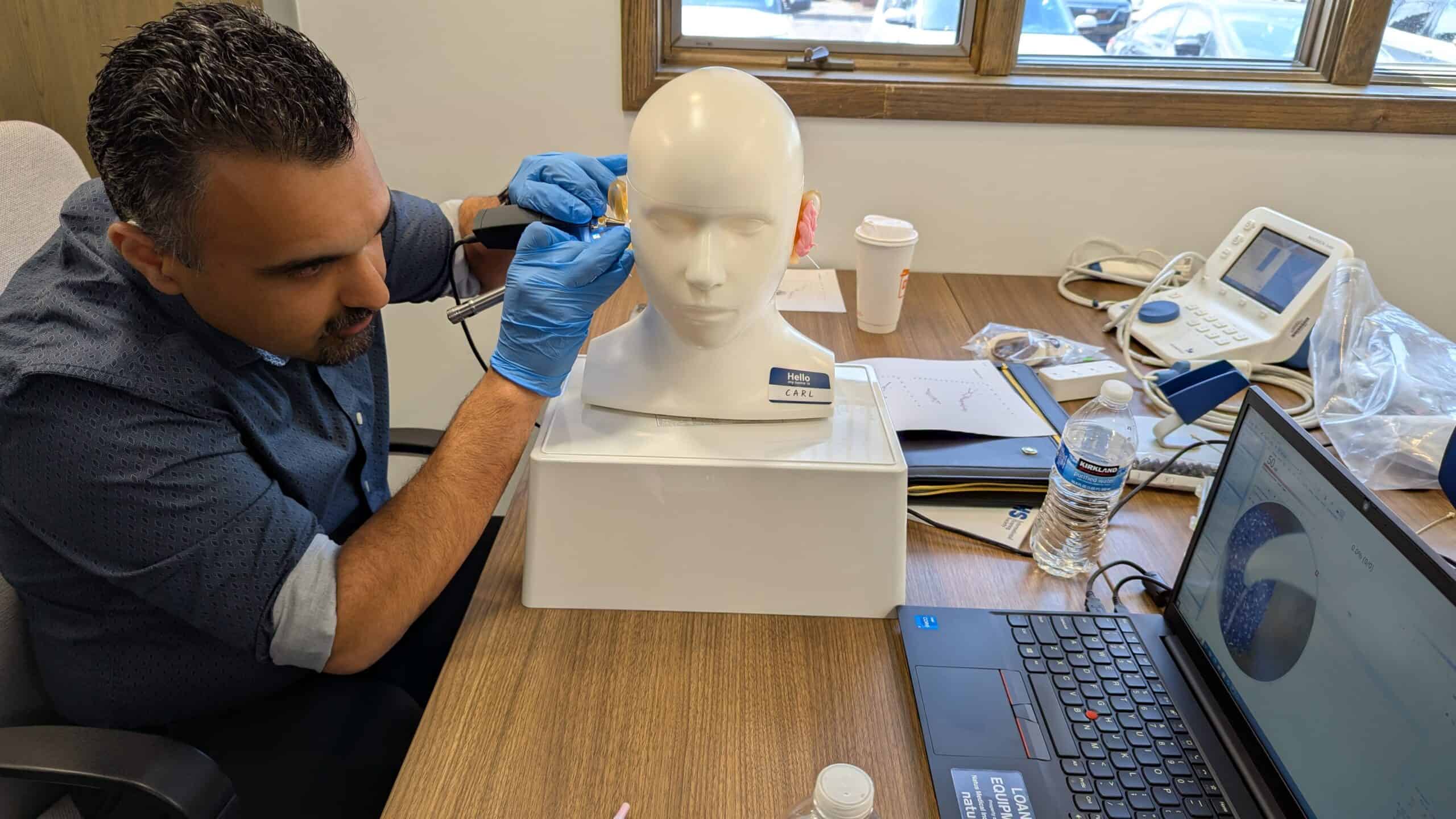 Hearing care professional adjusts a hearing aid on a mannequin.