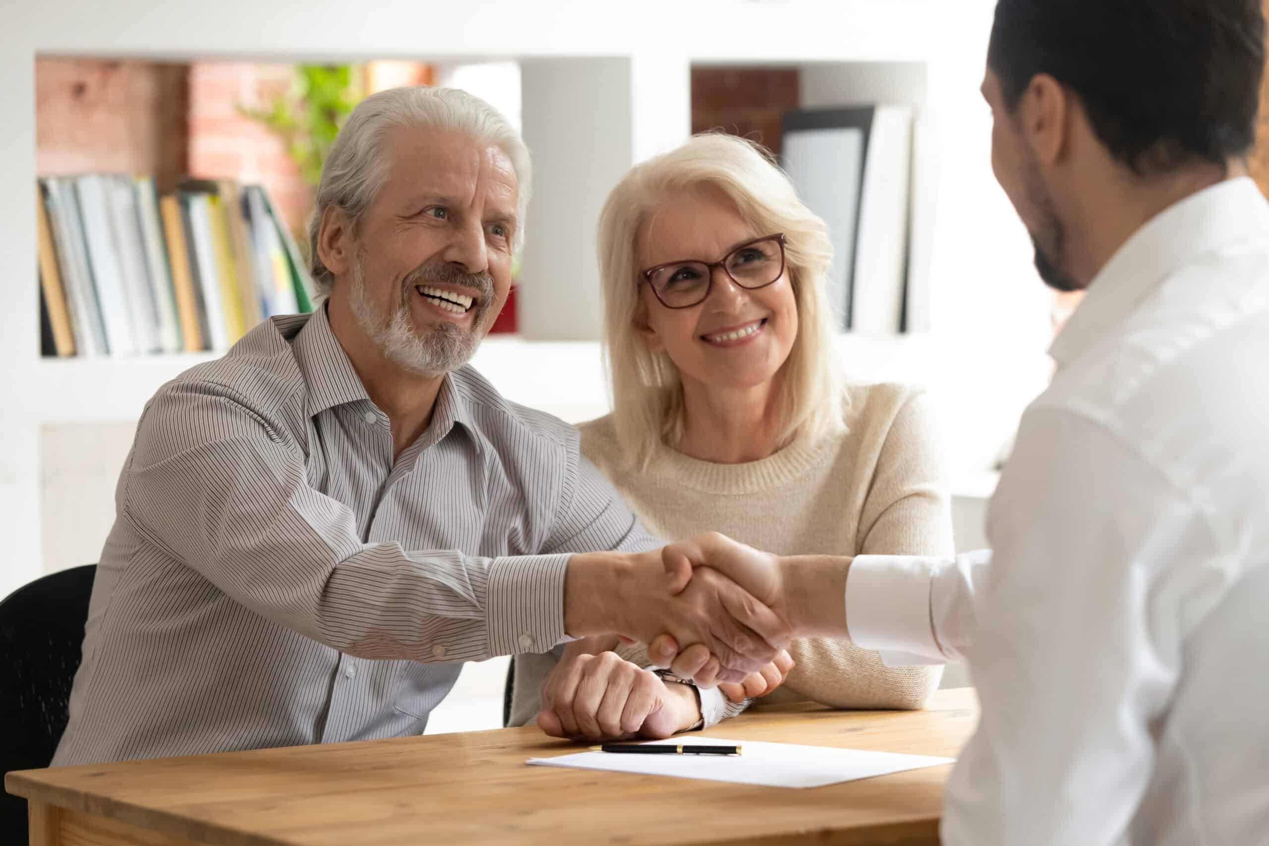 a man and a woman smiling at a professional across the table. The man is shaking the professional's hand