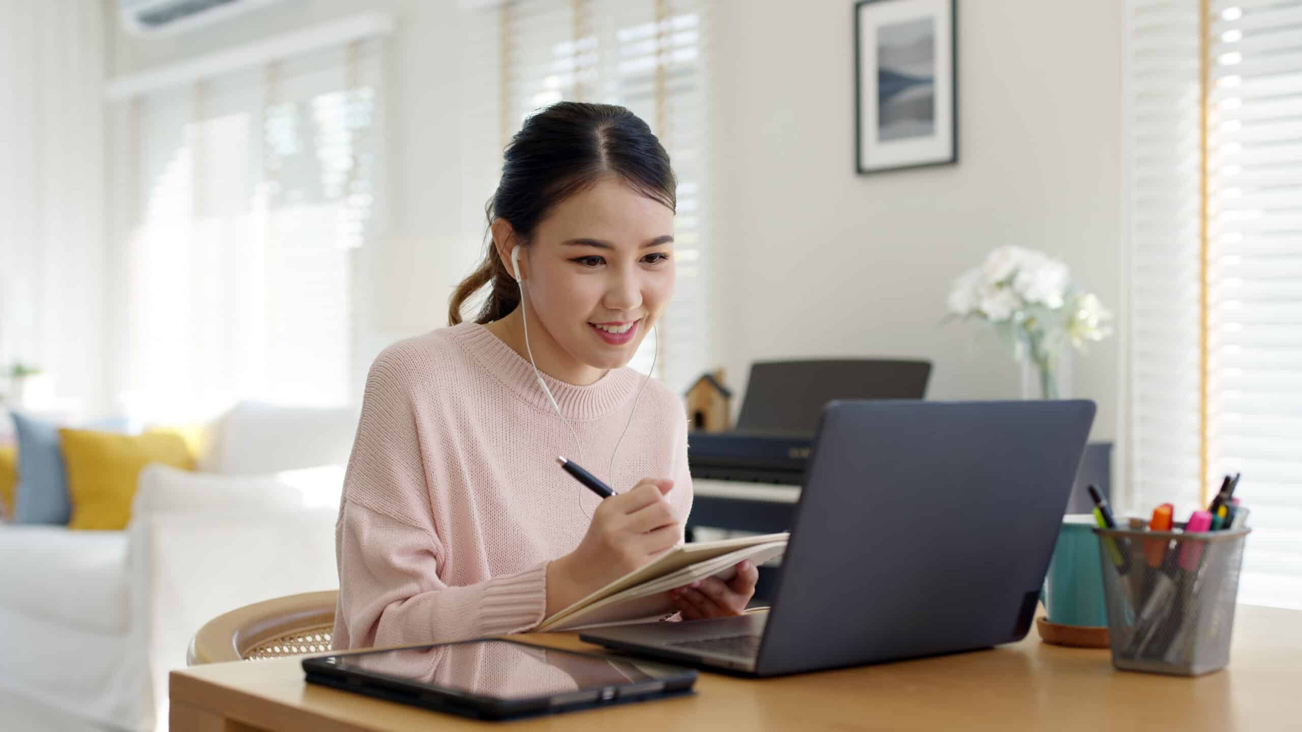 Woman takes notes while on a laptop.