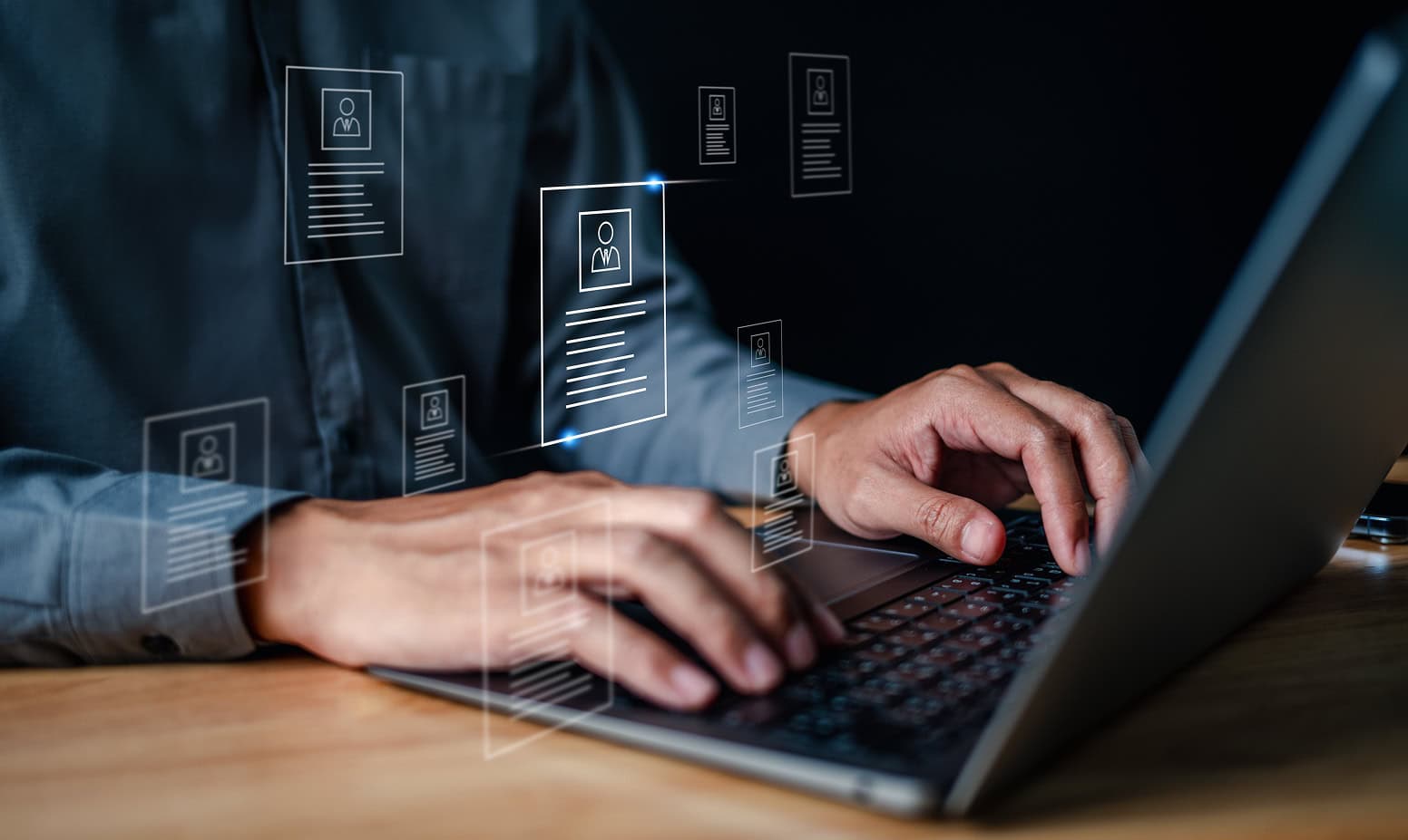 Close-up of hands typing on a laptop keyboard, with transparent digital profile icons and document graphics overlaid, suggesting online resumes, data management, or digital recruitment technology.