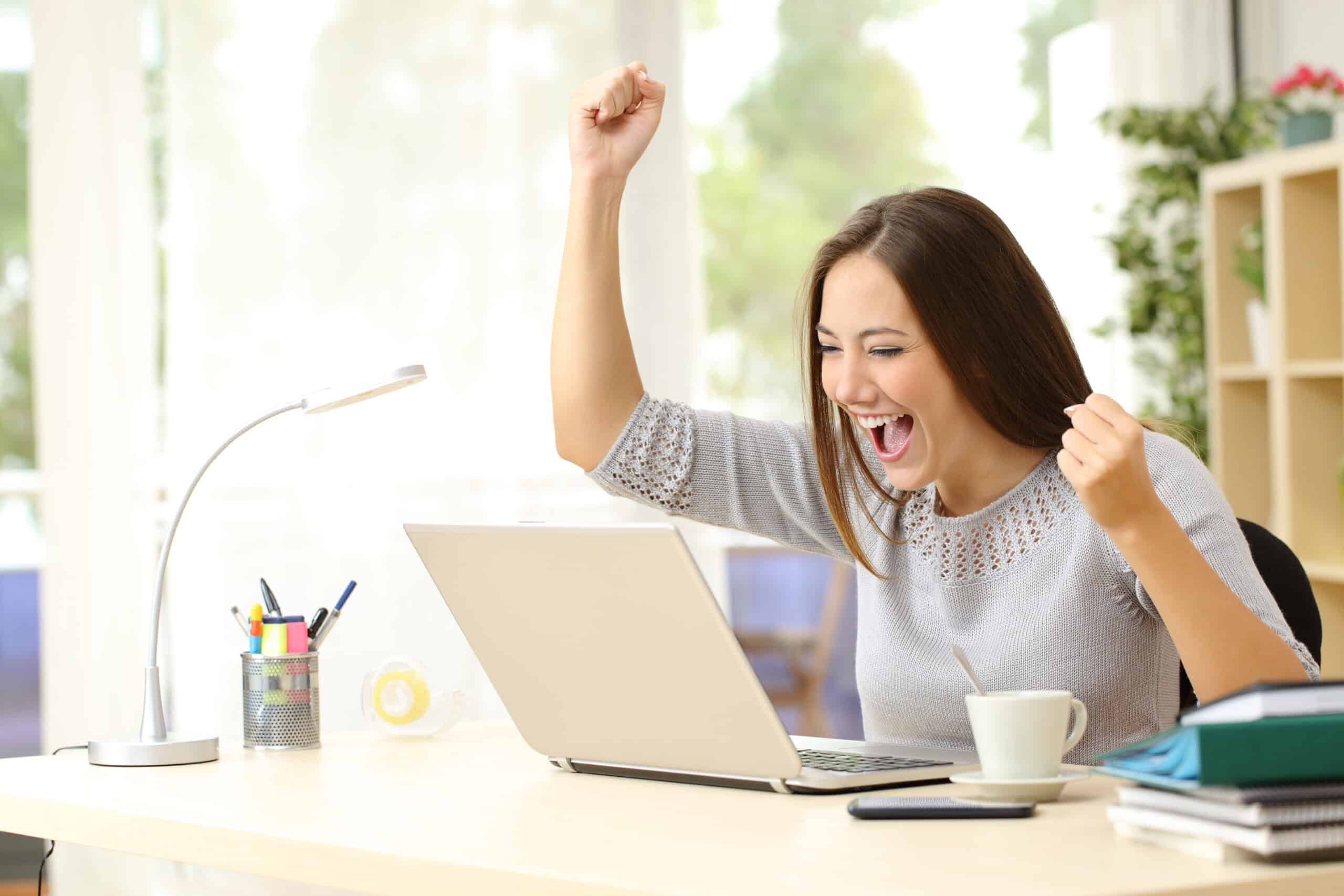 woman sitting in front of a computer and excited with hands in the air