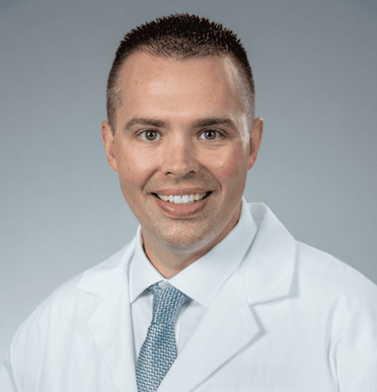 Portrait of Ben Norris wearing a white coat and blue tie.