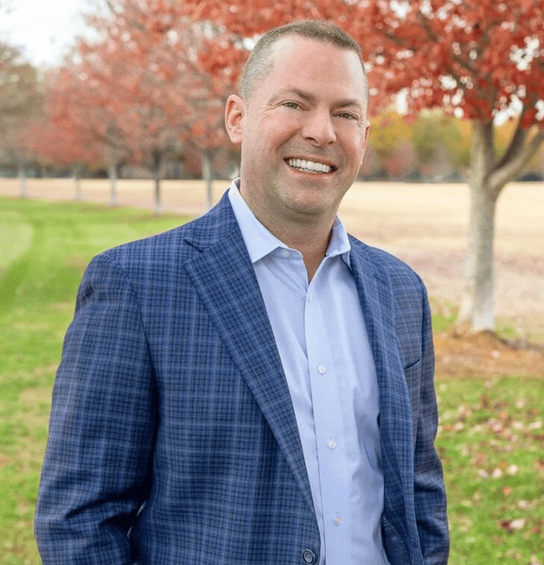 Jason Orsik in blue blazer smiling outdoors in autumn.