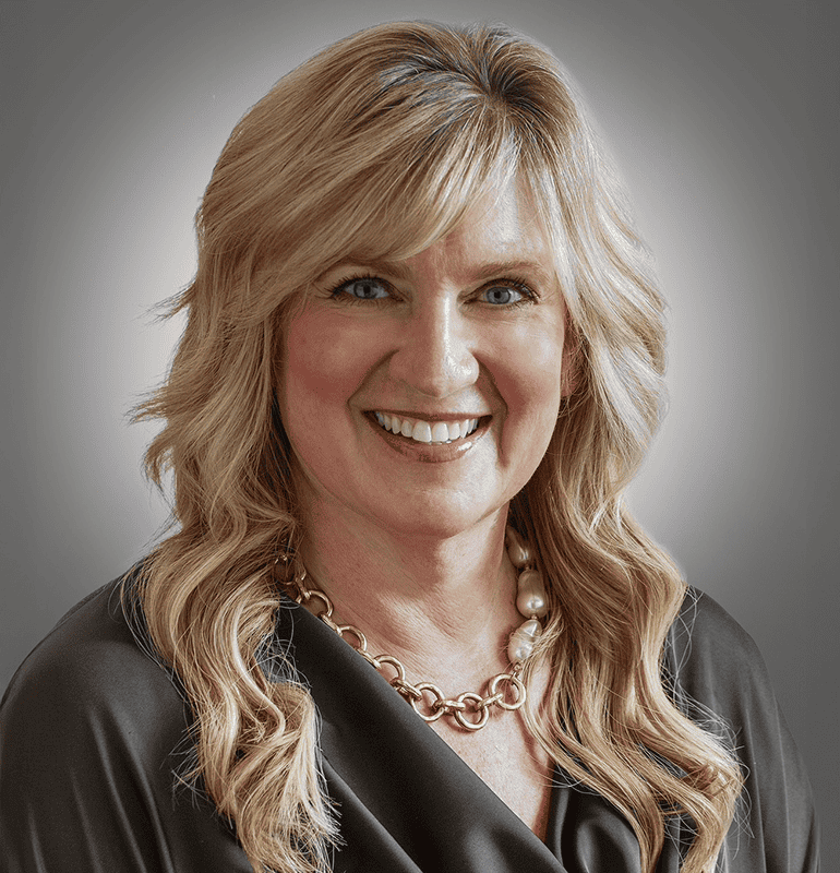 Julie Duensing smiling, wearing gold chain necklace.