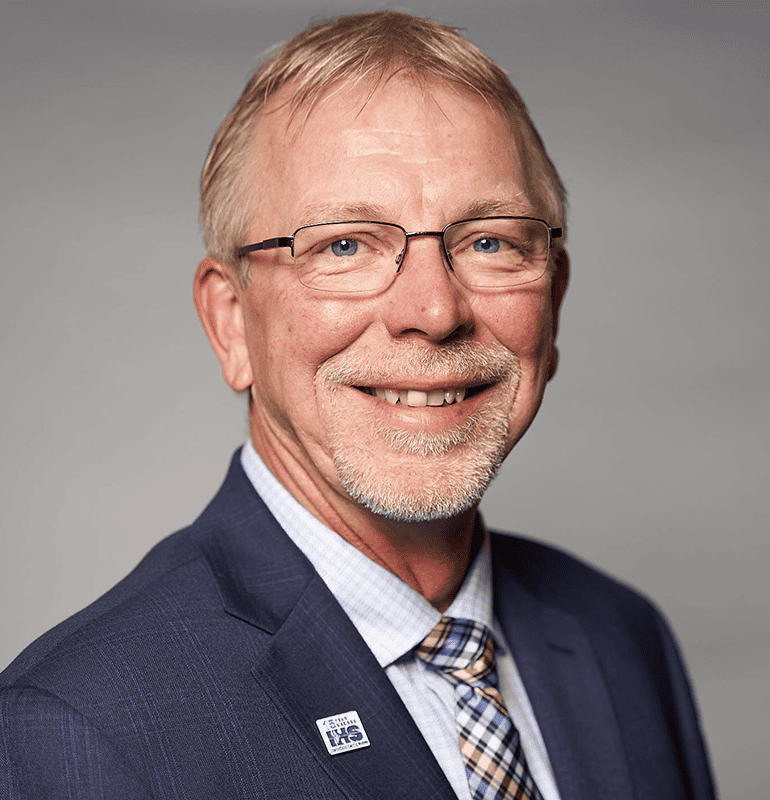 Michael K. Stone, BC-HIS, smiling in a suit with a blue and white patterned tie.