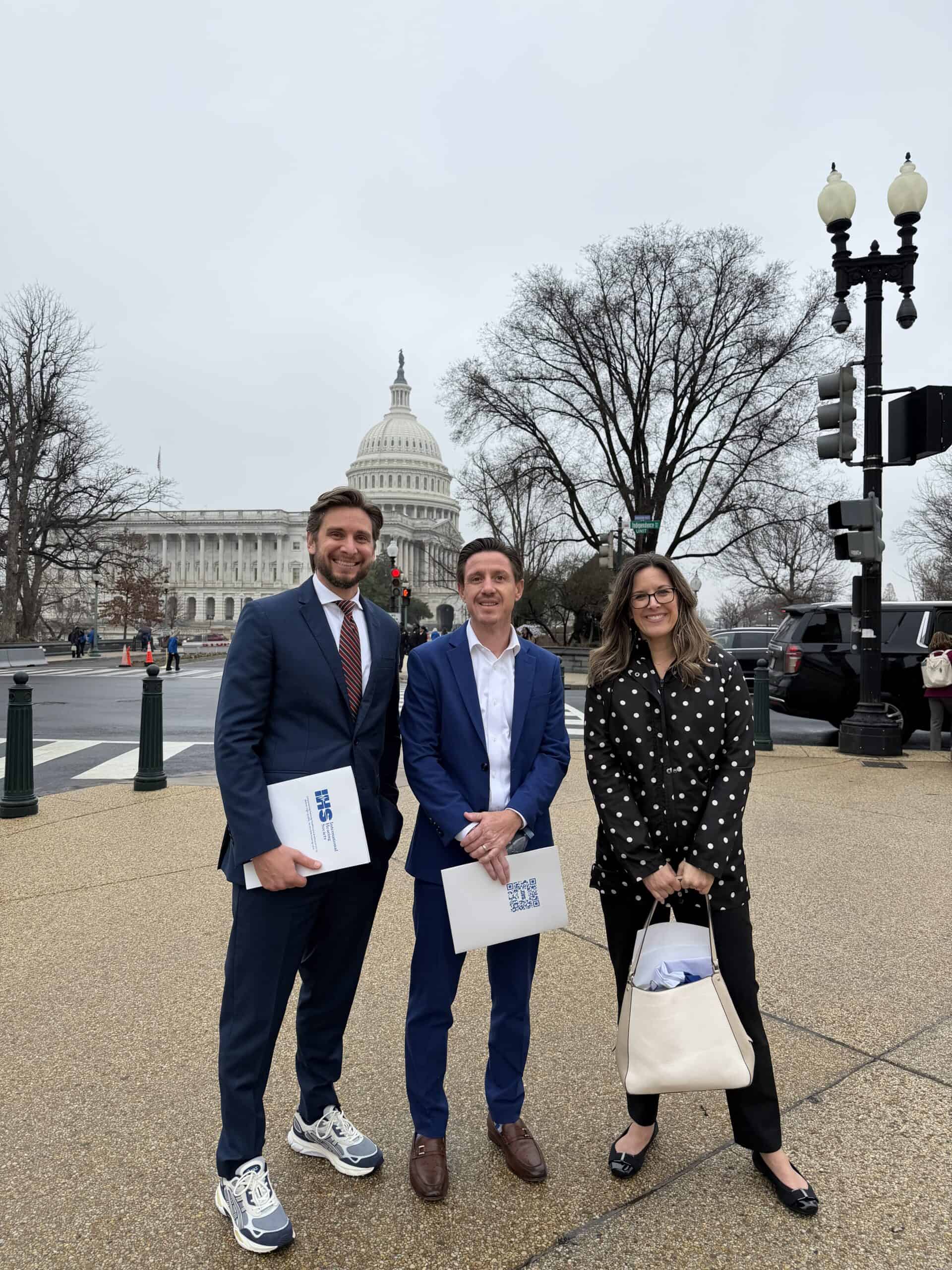Advocates on Capitol Hill holding IHS reports. US Capitol Building in background.