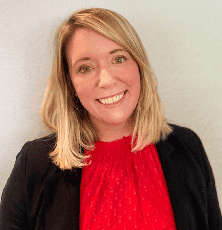Dr. Laura Lassen, AuD, smiles wearing a black blazer and red top.