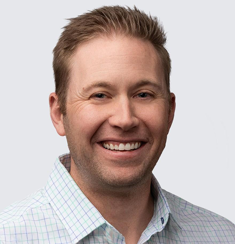 Portrait of Brendan Sullivan, smiling in a light blue and green checkered shirt.