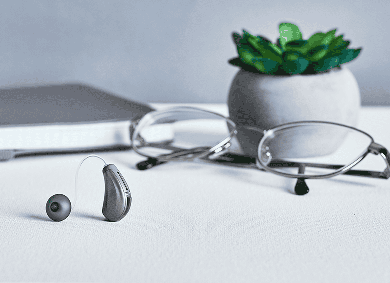 Hearing aid, glasses, and notebook on a desk