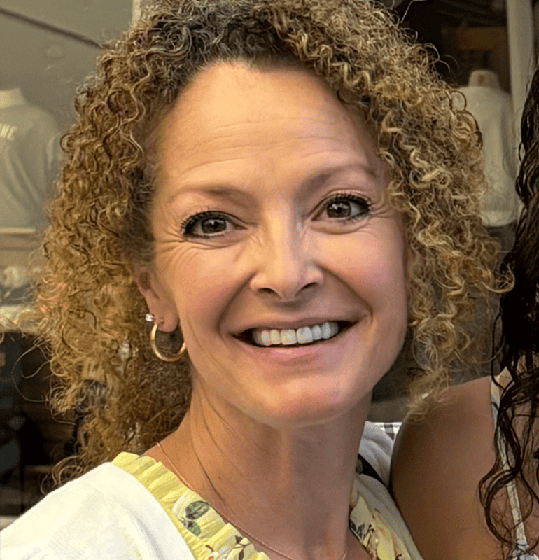 Woman with curly blonde hair smiling in a white cardigan